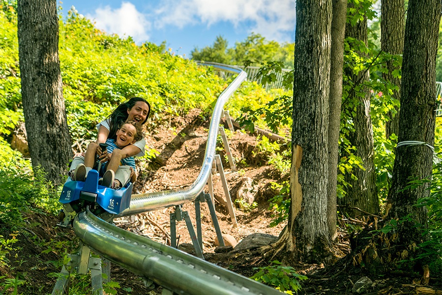 Smiling woman and child riding pipe coaster through forested terrain