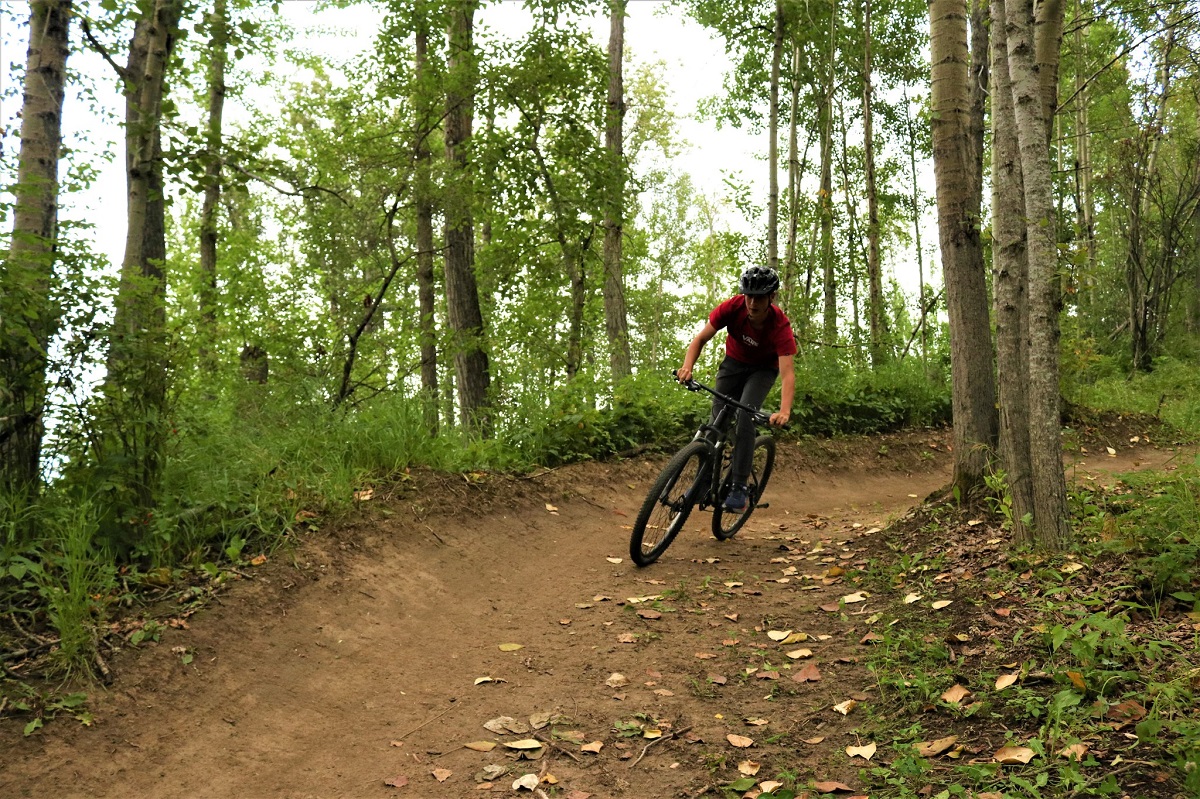 Adolescent in red tshirt mountain biking on dirt trail through forest