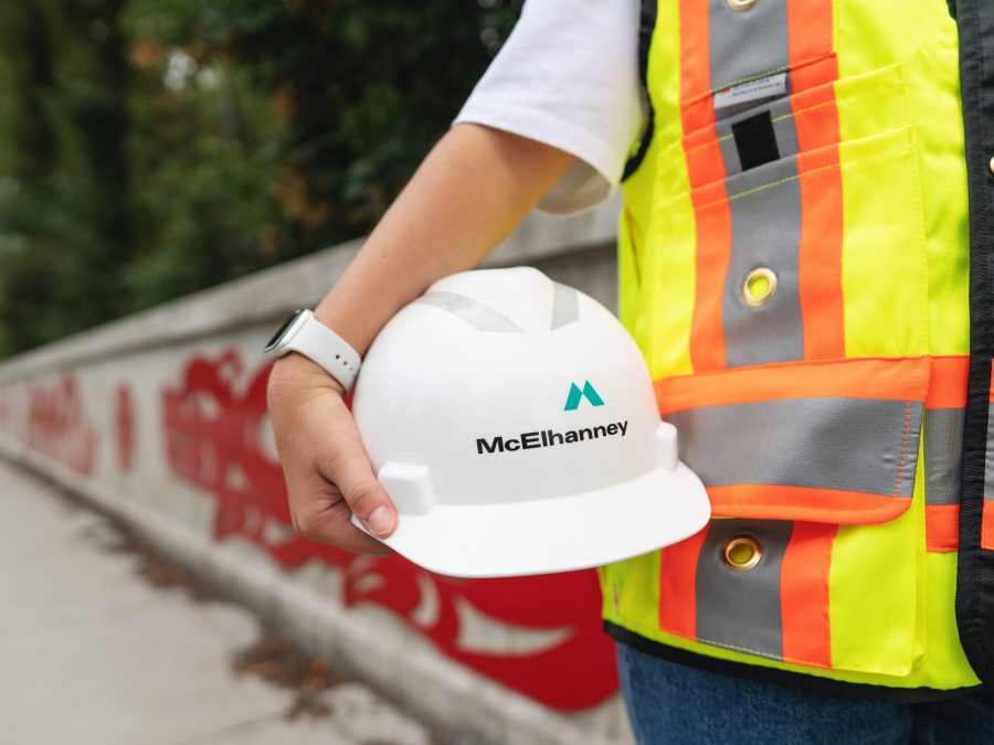 McElhanney helmet held in front of indigenous motifs mural