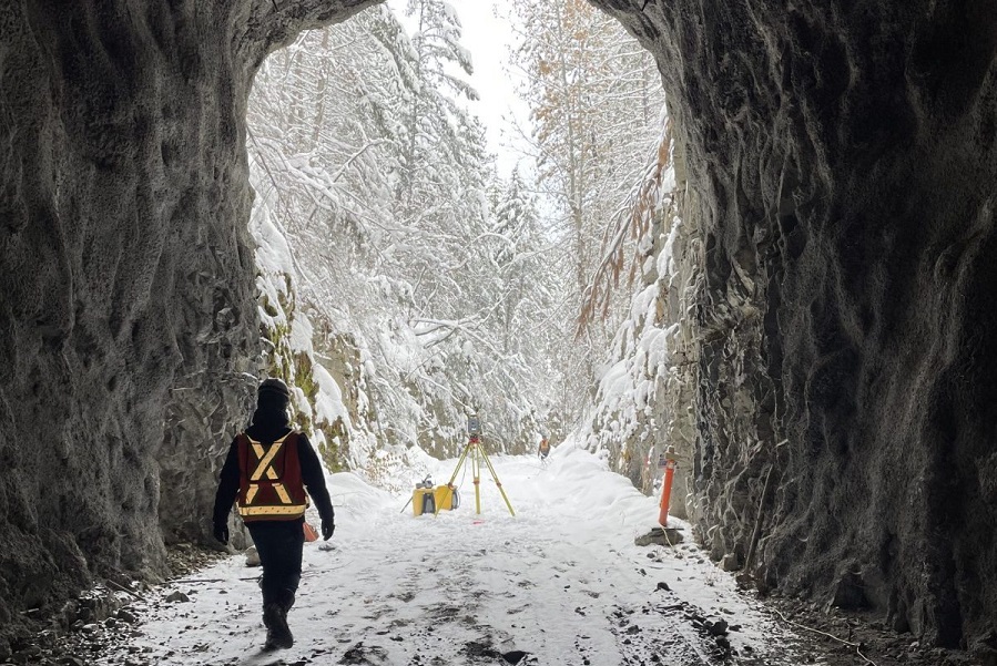 Person in safety vest walking out of underground tunnel towards a wintery forest.
