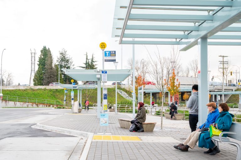 People waiting at bus shelters within the upgraded Phibbs Transit Exchange, showing accessible seating, covered walkways, and improved pedestrian spaces.