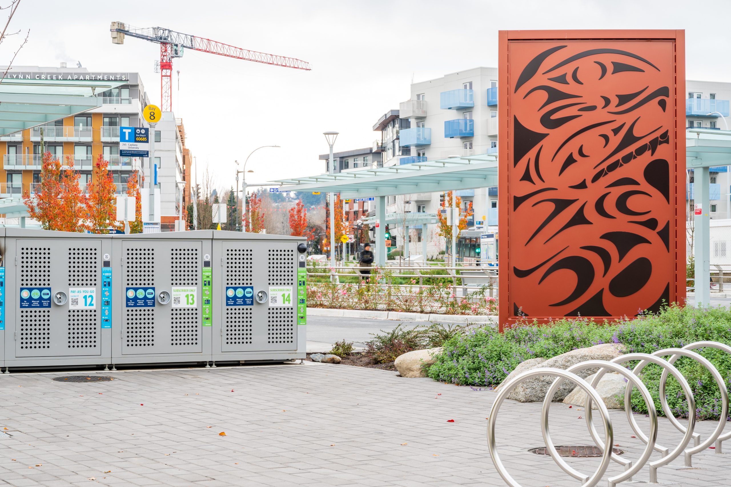 Bike storage lockers and a public art feature at the Phibbs Transit Exchange with transit shelters in the background.