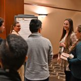 A group of people is gathered in a conference room and is sharing discussion around a flip chart.