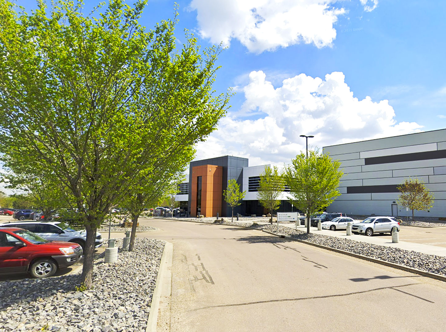 Alberta Gaming and Liquor Distribution Centre A view of the Alberta Gaming and Liquor Distribution Centre from Google Maps Street View, showing a modern building with a mix of grey and orange exterior, surrounded by trees and parked cars under a partly cloudy sky.