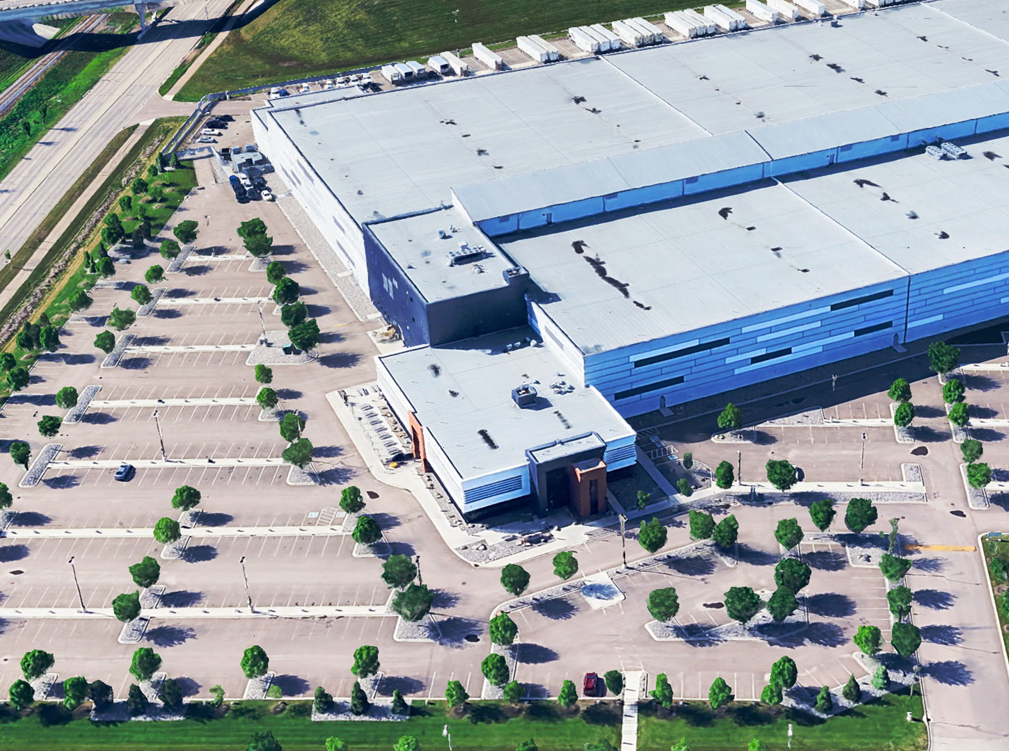 Aerial View of Alberta Gaming and Liquor Distribution Centre Aerial view of a large warehouse-style building with a flat roof, loading docks, and a surrounding parking lot with trees and green spaces, likely located in an industrial park.