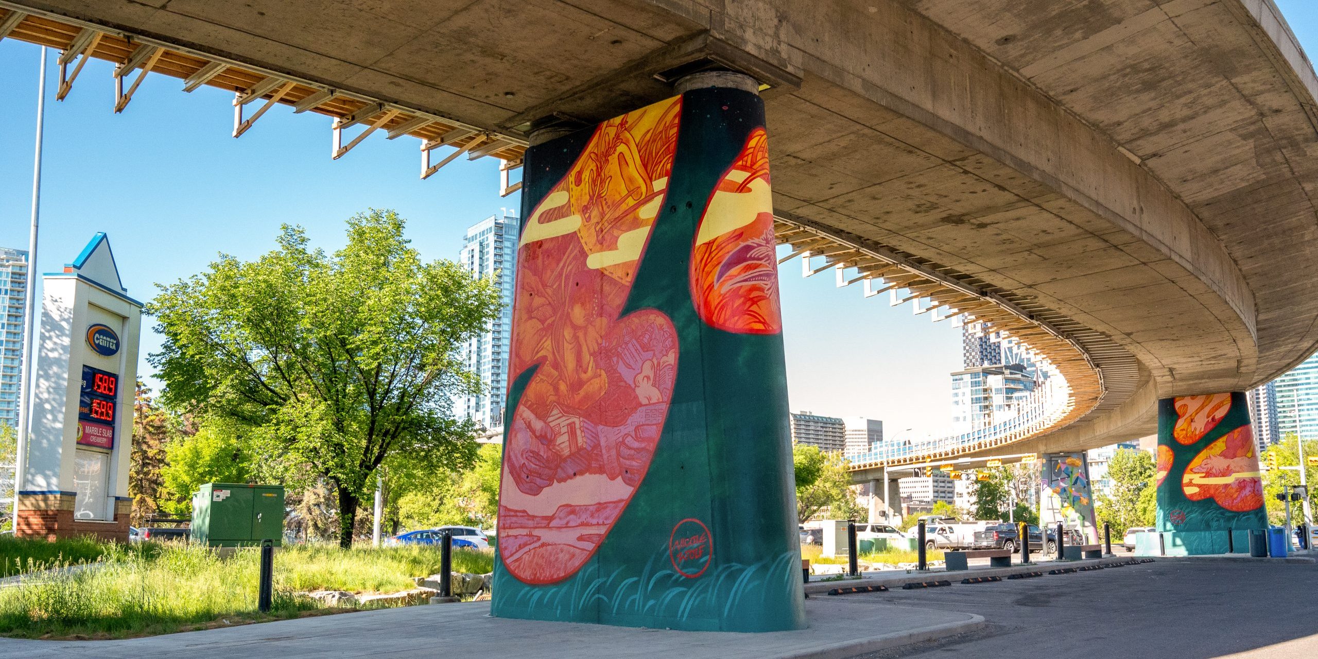 Colorful mural painted on concrete pillars beneath an overpass in a city, with bright designs adding vibrancy to the urban streetscape.