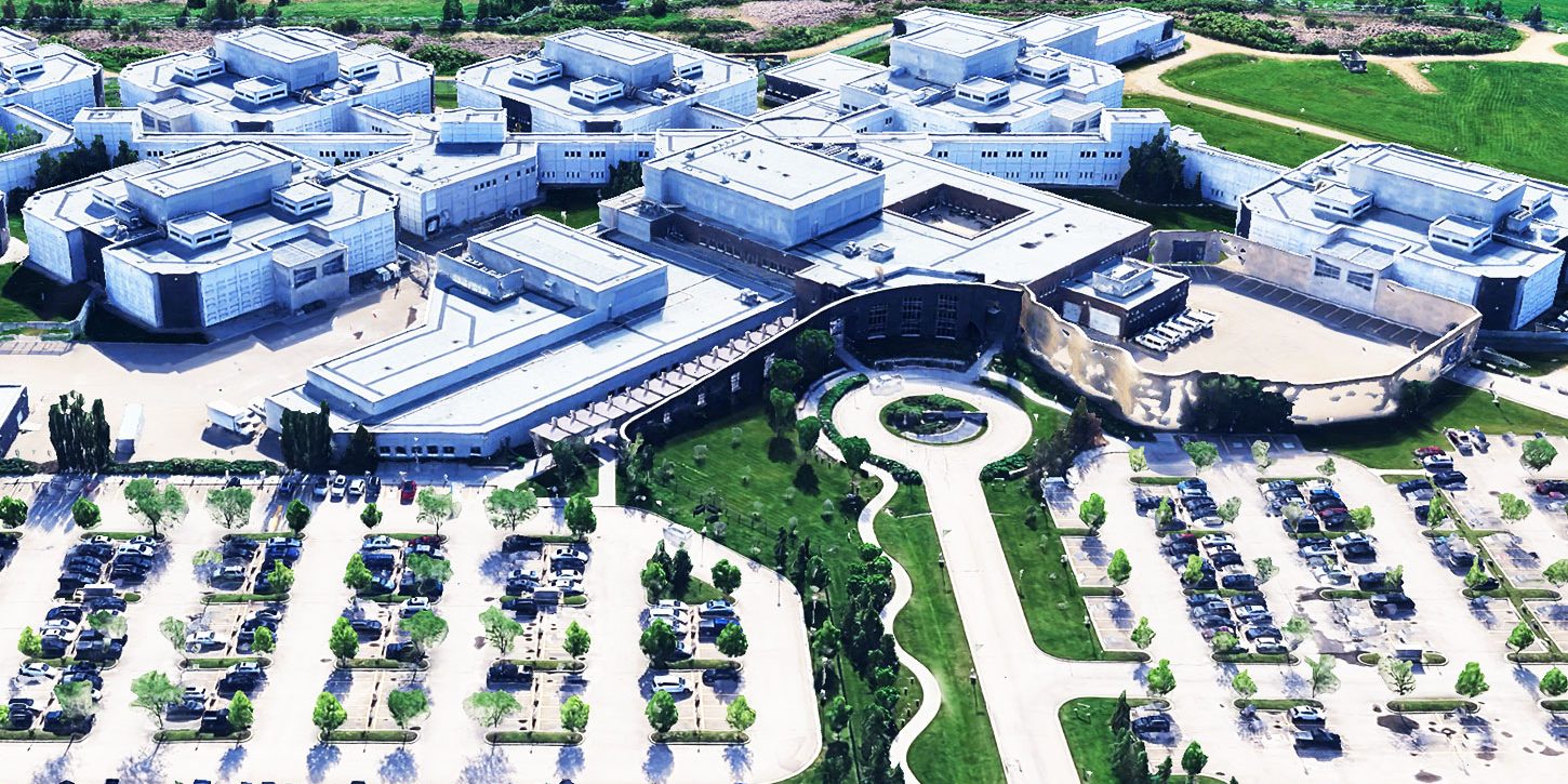 Aerial view of the Edmonton Remand Centre showing a large complex with multiple interconnected buildings, parking lots, green spaces, and surrounding natural landscape.