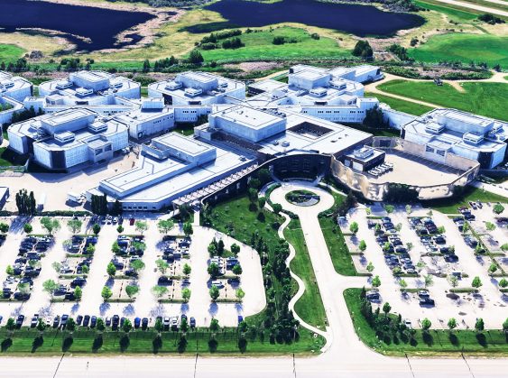 Aerial view of the Edmonton Remand Centre showing a large complex with multiple interconnected buildings, parking lots, green spaces, and surrounding natural landscape.