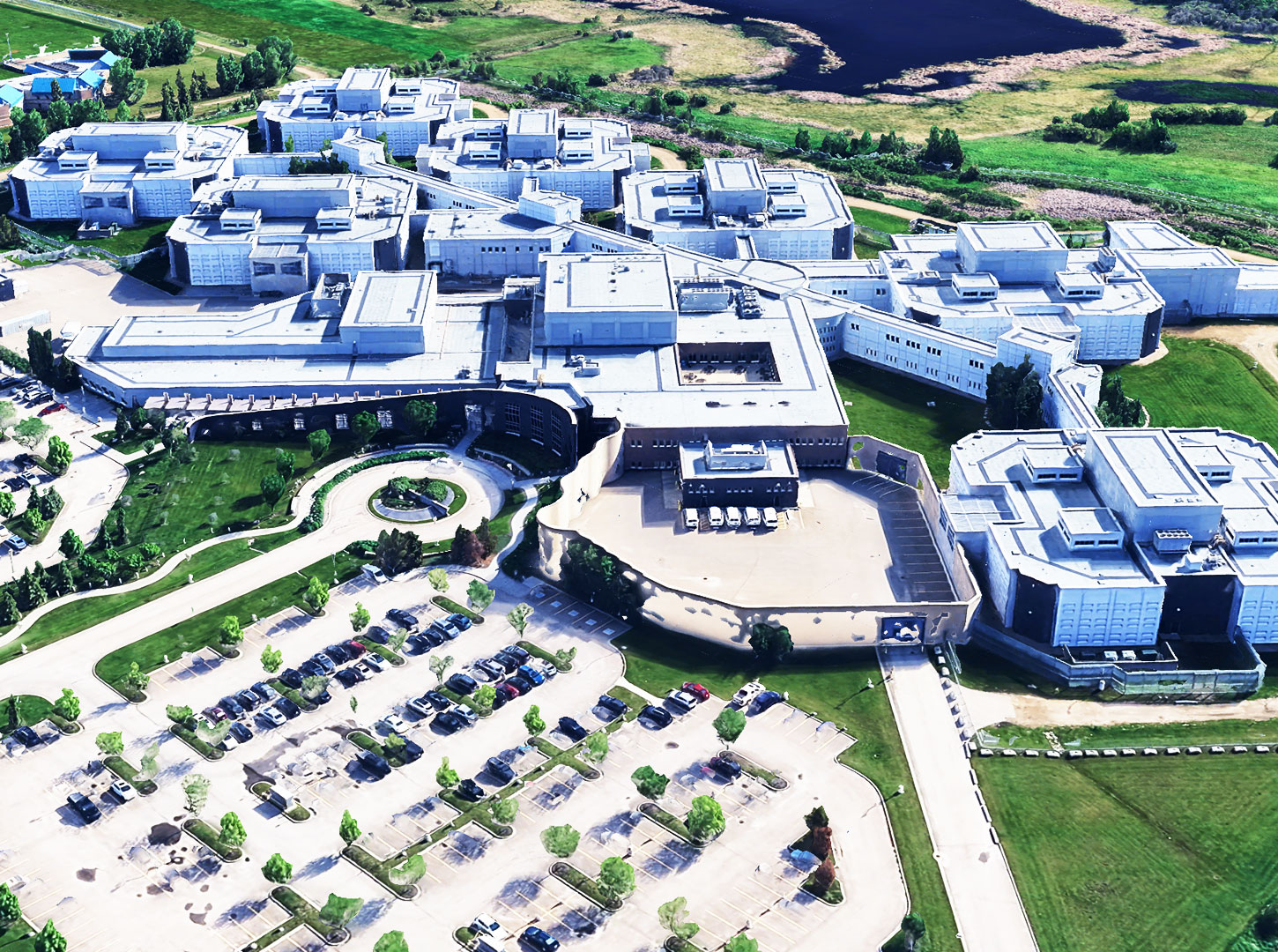 Edmonton Remand Centre – Architectural Layout from Above Aerial rendering of the Edmonton Remand Centre focusing on the structural layout of the buildings, parking areas, and adjacent green zones.