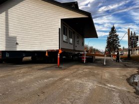 Modular housing unit being transported across excavation site.