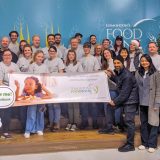 Over two dozen people in matching tshirts gather around a sign celebrating McElhanney’s involvement in a local charity.