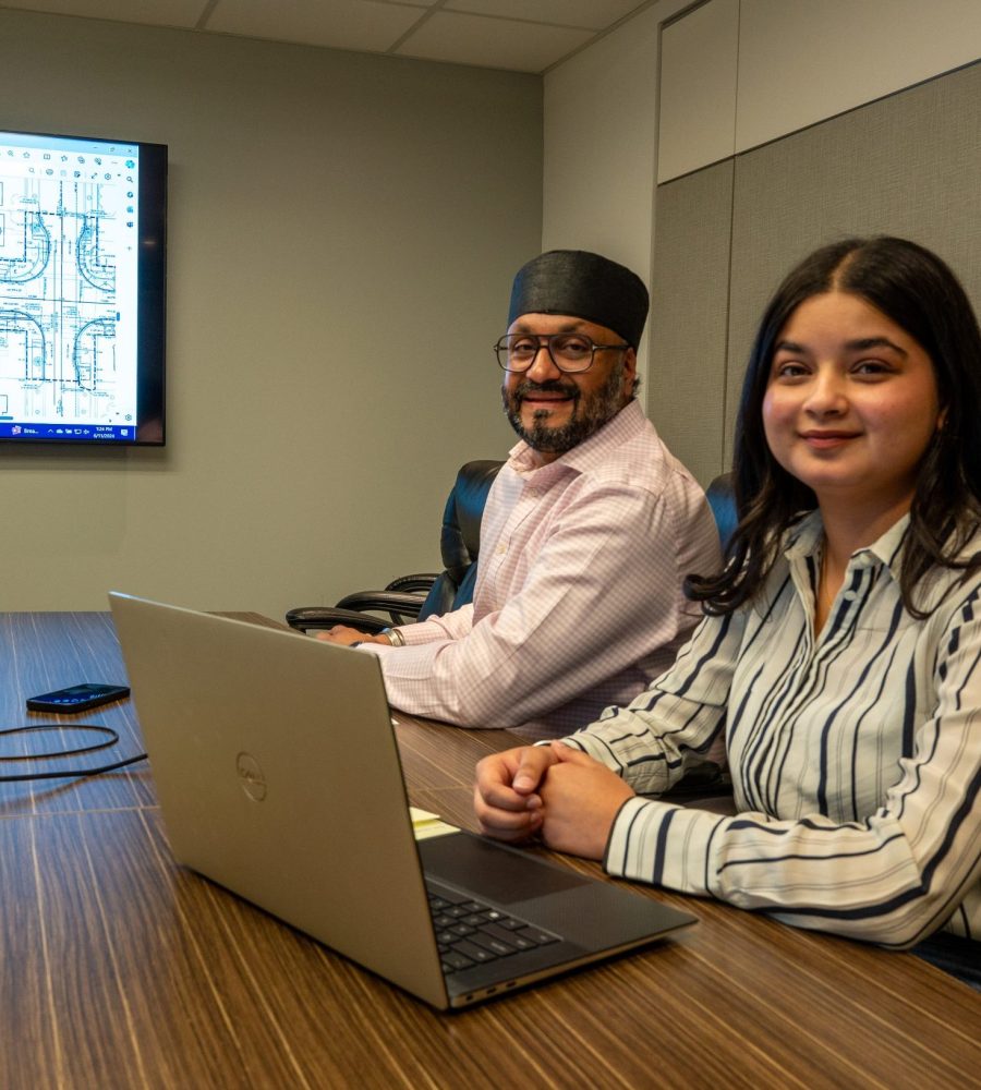 Two colleagues collaborate in a meeting room during a mentorship discussion, reviewing technical plans on a shared screen.