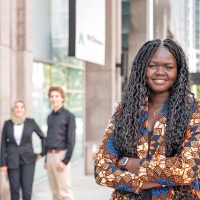 A young person stands in the foreground of the image, smiling into the camera. Three individuals are gathered in the background, chatting with one another.