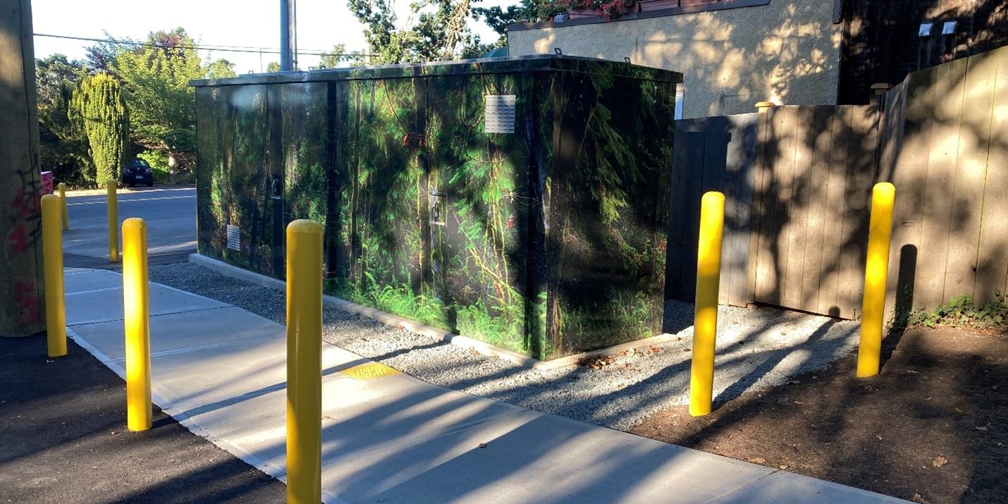 Aboveground PRV kiosk at the Wilkinson–Burnside site, surrounded by protective bollards, with multiple access doors and a nature‑themed exterior wrap.