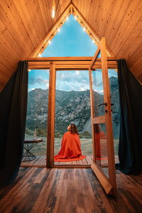 Person seated inside a wood-framed glamping cabin overlooking a mountain landscape
