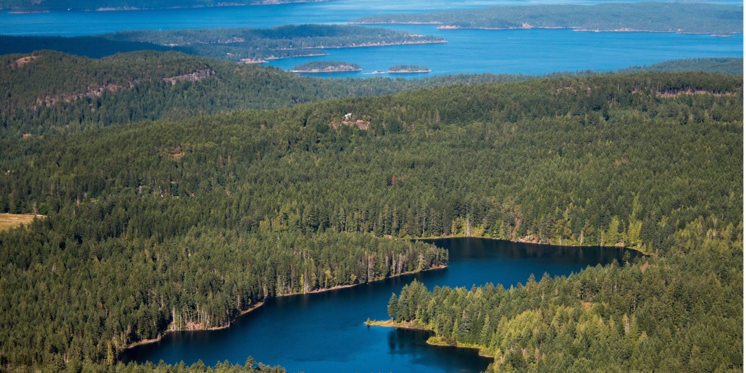 Aerial view of coastal forest with islands, lake, and blue ocean in the background.