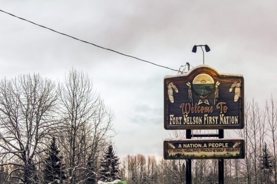 Sign reading “Welcome to Fort Nelson First Nation” with trees and sky in the background.