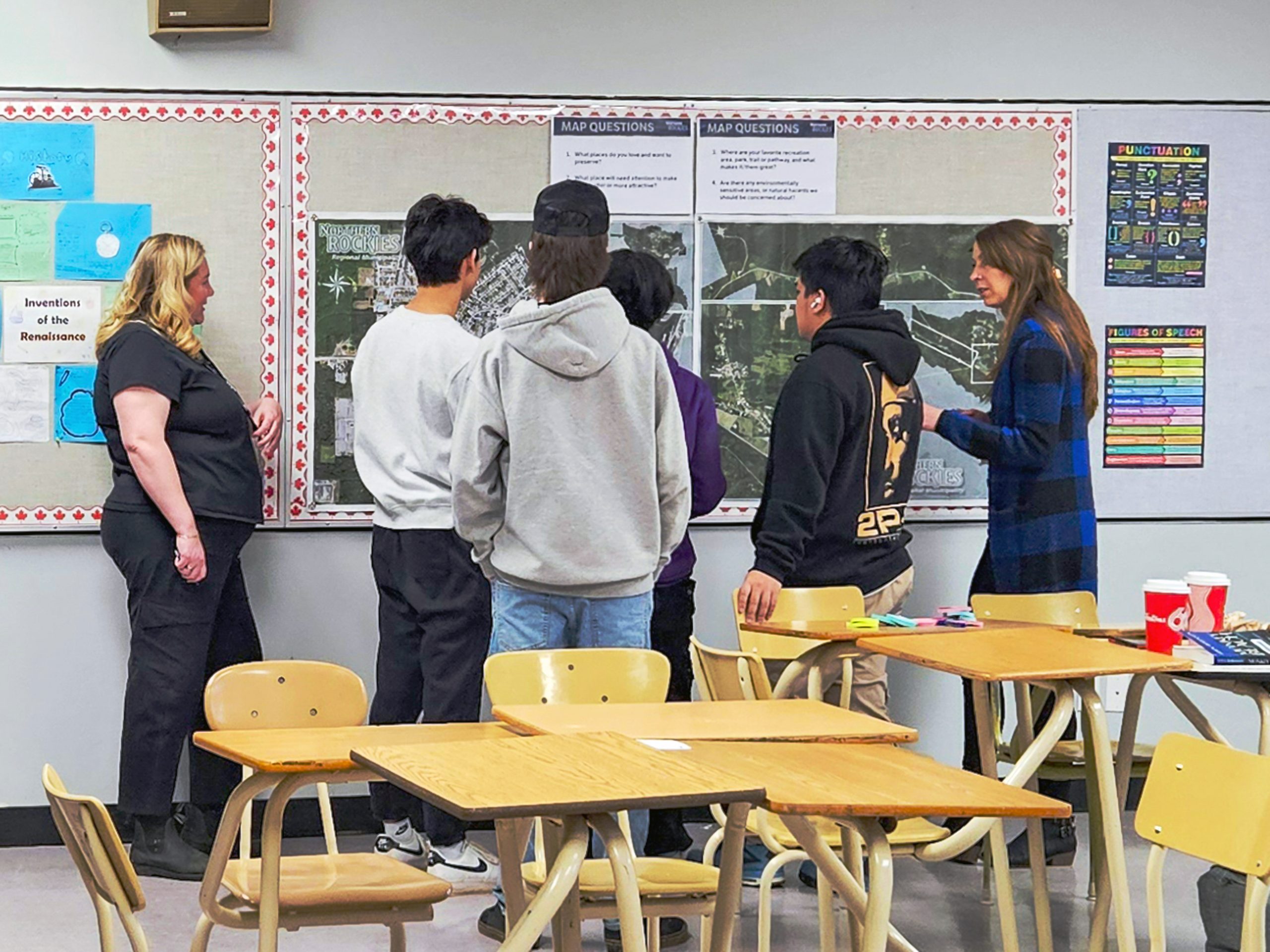 Group gathered around wall-mounted maps discussing community planning information in a classroom setting
