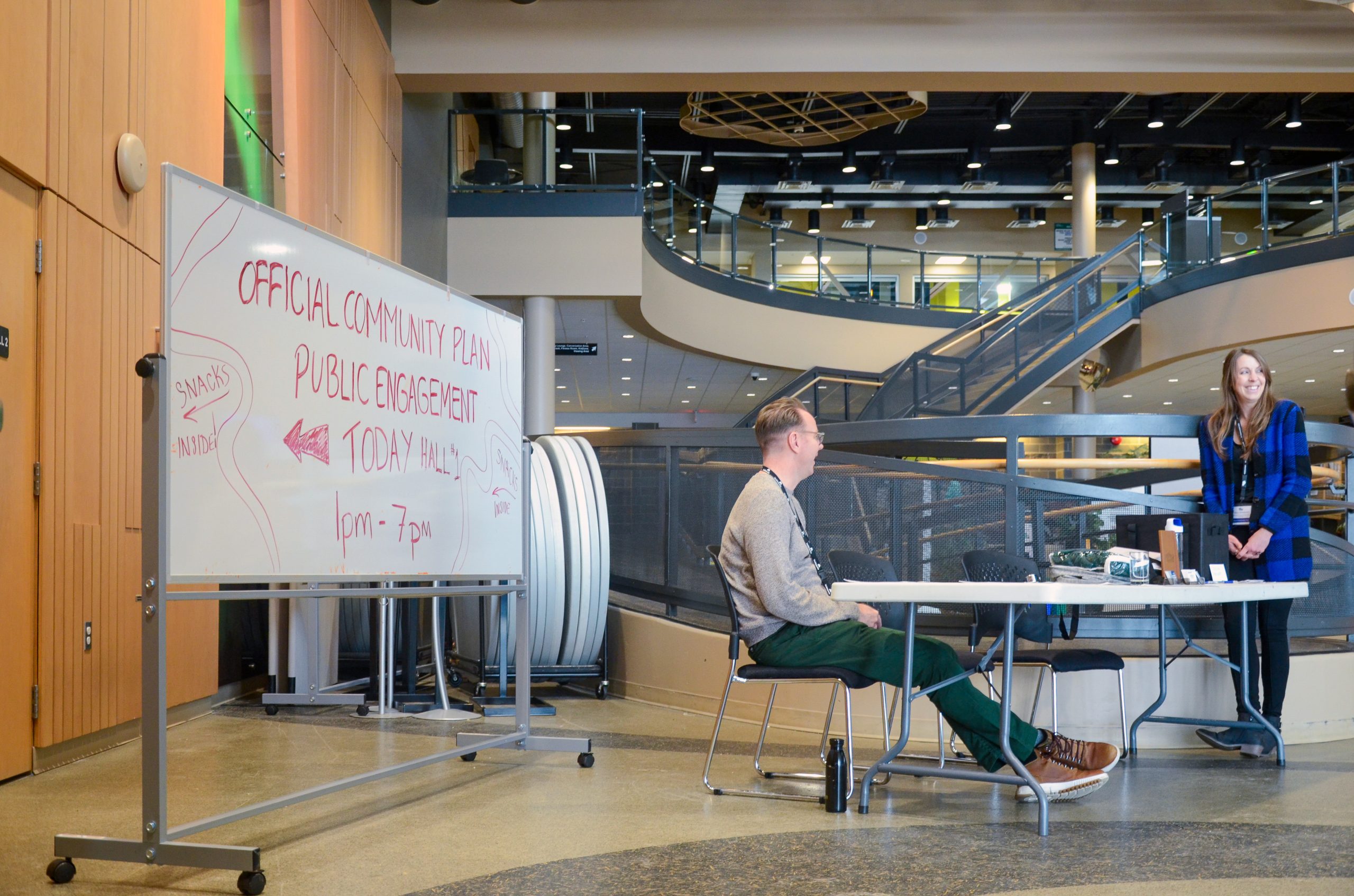 Indoor space with a whiteboard reading “Official Community Plan Public Engagement” beside a table set up for discussion