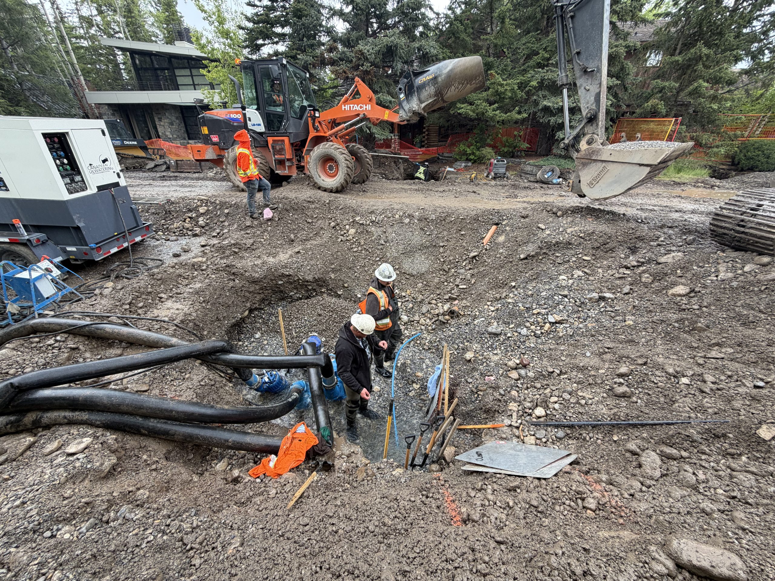 Underground water infrastructure installation Construction crew installs underground water infrastructure using excavation and dewatering system, with excavator and pumps on an urban job site.