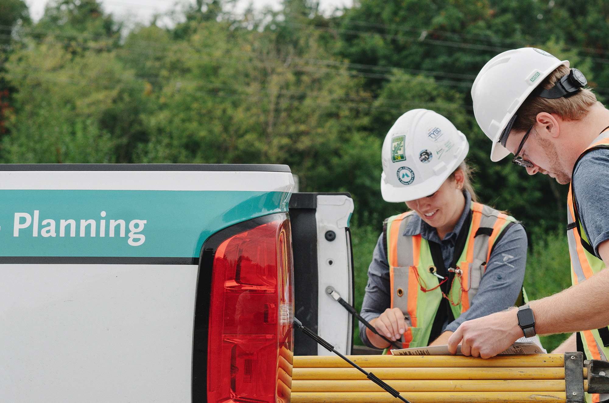 McElhanney services Two workers in PPE reviewing materials on the tailgate of a truck.