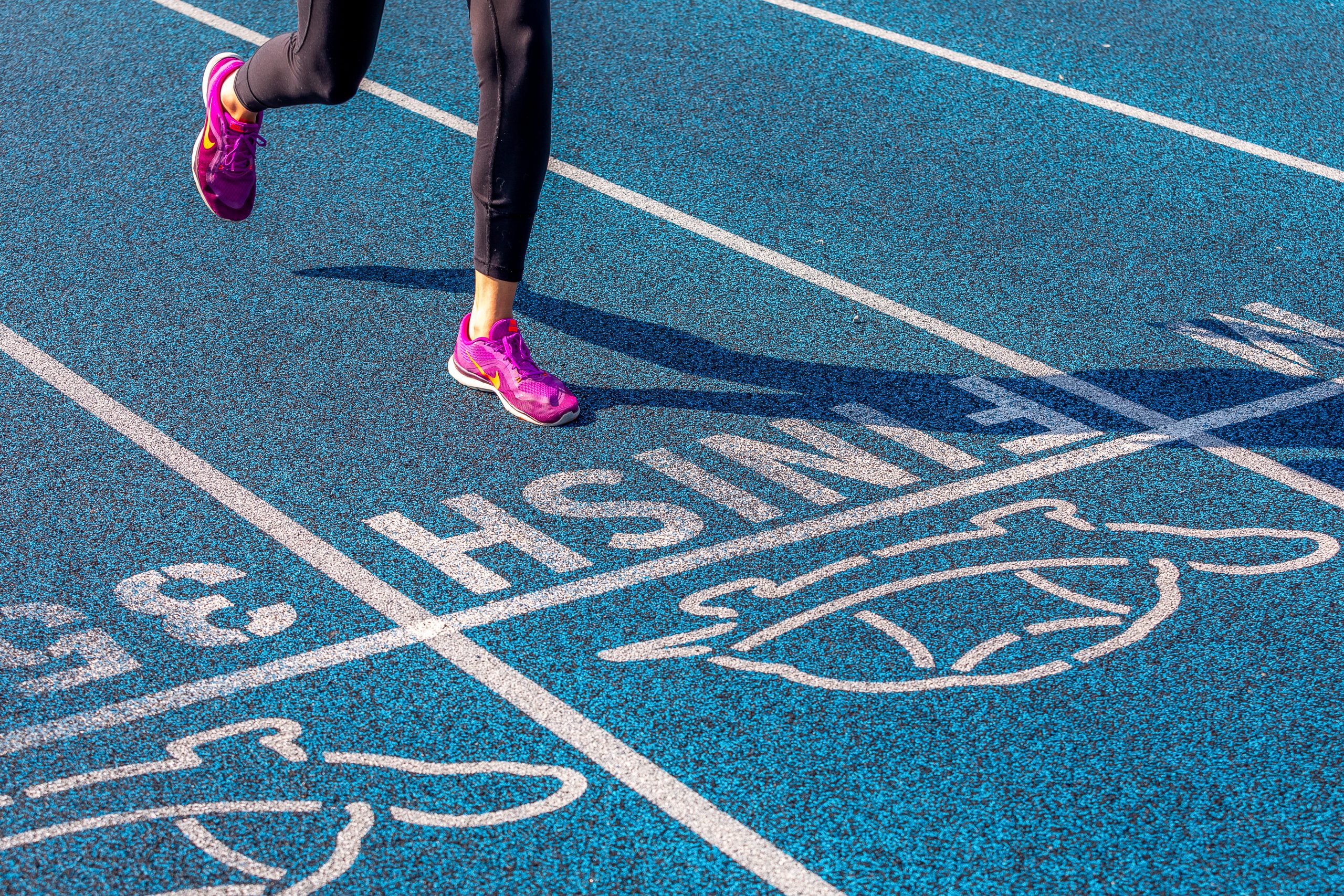Runner in athletic gear reaches finish line on blue, outdoor track Runner in athletic gear reaches finish line on blue, outdoor track